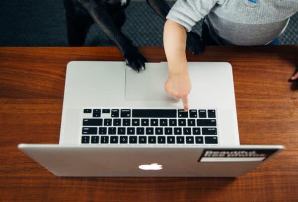 Child pointing at laptop keyboard during work from home setup, emphasizing ergonomic practices.